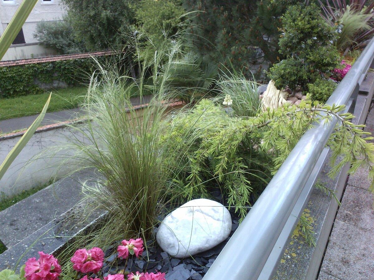 Jardinière de balcon avec fleurs roses, graminées et un galet blanc