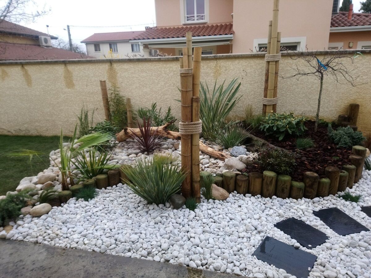 Parterre de galets blancs, rondins et bambous le long d'un mur, avec dalles en ardoise